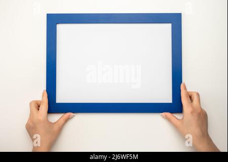 Nachbau des Haltrahmens. Foto-Mockup. Frau Hände halten blauen Rahmen. Für Rahmen- und Poster-Design. Rahmengröße A4. Isoliert auf weißem Hintergrund. Blank pho Stockfoto