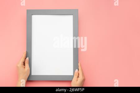 Ein Fotorahmen-Modell an einer rosa Wand hängen. Bild-Frame-Modell. Frau halten leere Diplomrahmen auf rosa Wand Hintergrund. Verkürzte Hand einer Frau, die hält Stockfoto