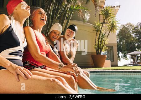 Eine Gruppe von Senioren lacht fröhlich, während sie sich am Pool entspannen. Fröhliche ältere Menschen genießen ihren Sommerurlaub in einem Kurort. Stockfoto