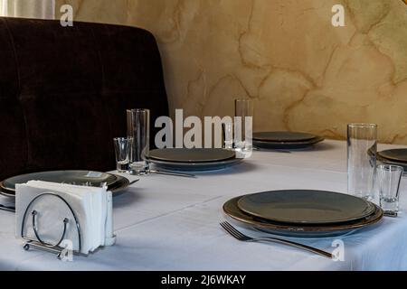 Tabelleneinstellung. Glas, Stapel, Schüsseln und Gabel auf dem Tisch. Besteck auf einer weißen Tischdecke Stockfoto