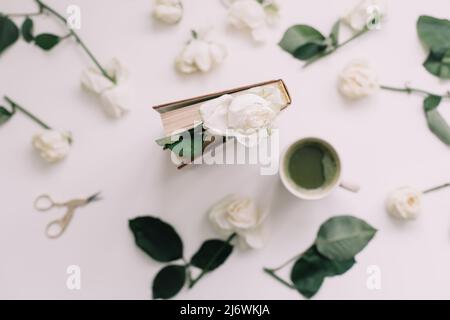 Ein Buch mit weißen Rosen und einer Tasse grünem Tee auf weißem Hintergrund, Draufsicht, Flatlay Stockfoto