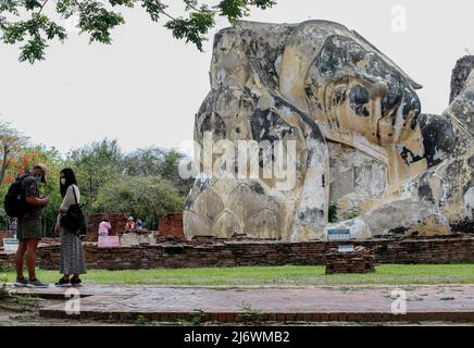 Ayutthaya, Thailand - am 4. Mai 2022 Besucht Ein Touristenpaar mit Gesichtsmasken als vorbeugende Maßnahme gegen die Ausbreitung des Coronavirus einen liegenden Buddha im Wat Lokayasutharam Tempel in Ayutthaya, nördlich von Bangkok. Stockfoto