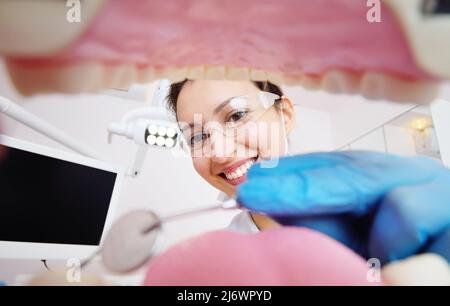 Die hübsche junge Zahnärztin untersucht die Zähne des Patienten. Blick von der Innenseite des Kiefers. Stockfoto