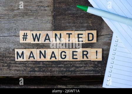 Holzspielzeugblöcke mit dem Text Wanted Manager darauf mit Stift und Papier im Hintergrund. Perfekte Aufnahme für Recruiter, Personalabteilung, Unternehmen und Unternehmen Stockfoto