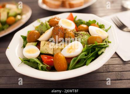 Frischer Salat aus Rucola, Avocado, Kirschtomaten mit Oliven und Wachteleiern in einer weißen Schüssel Stockfoto
