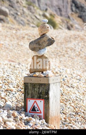 Steinbalancierung an einem felsigen Strand mit einem Warnschild für herabfallende Steine. Stockfoto