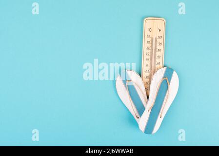 Leerer blauer Hintergrund mit Thermometer und Flip Flops, Urlaubshintergrund, Sommerurlaub, heißes Wetter, Strandartikel Stockfoto