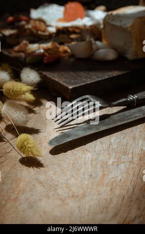 Vintage altes Metallmesser mit Gabel und getrockneten Kaninchen Schwanz Gras Blumen auf alten rustikalen Holz Esstisch. Esskonzept, Kopierraum, selektiver Fokus. Stockfoto