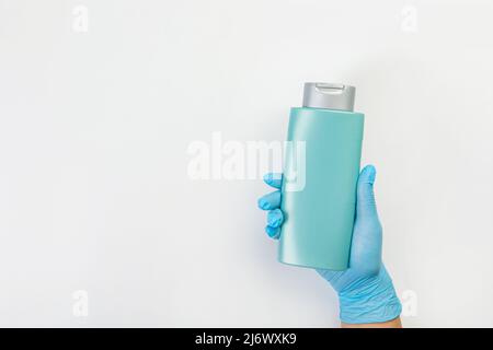 Die Hand einer Putzfrau in einem blauen Gummihandschuh hält eine Flasche Reinigungsmittel auf einem grauen Hintergrund. Reinigungsmittel für verschiedene Oberflächen in der Küche Stockfoto