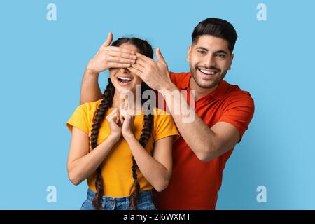 Hübscher junger arabischer Mann, der die Augen seiner Freundin mit Händen bedeckt und „Guess Who“ spielt Stockfoto