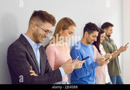 Eine Gruppe glücklicher junger Menschen, die Schlange stehen, ihr Handy benutzen und lächeln Stockfoto