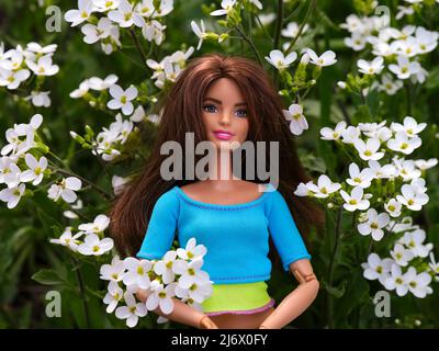 Tambow, Russische Föderation - 30. April 2022 Eine brünette Barbie-Puppe, die unter weißen Blumen im Freien steht. Stockfoto