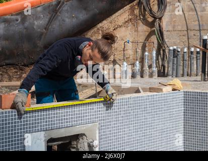 Junger Arbeiter, der in einem im Bau befindlichen Schwimmbad inmitten einer Baustelle Messungen annahm Stockfoto