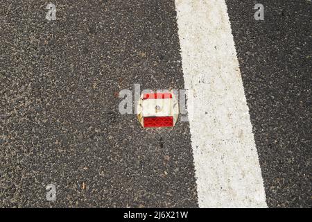 Metall-Straßenbolzen mit rotem Reflektor auf Asphaltstraße mit weiß lackierter Spurmarkierungslinie als Trennlinie auf nationaler Autobahnstraße in Indien Stockfoto