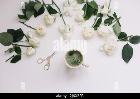 Eine Tasse grüner Tee mit weißen Rosen auf weißem Hintergrund von oben. Flatlay, Draufsicht, Kopierbereich. Stockfoto