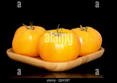 Drei gelbe, saftige Tomaten auf einem Bambustablett, Makro, isoliert auf schwarzem Hintergrund. Stockfoto