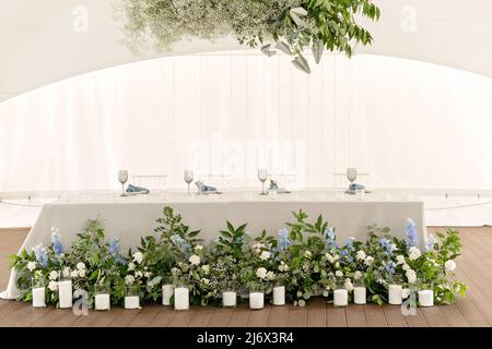 Hochzeitspresidium im Restaurant. Banketttisch für frisch Vermählte mit Blumen, Grün, Kerzen und Girlande-Ligths. Üppiges Blumenarrangement. Luxus-Weddi Stockfoto