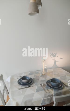 Gemütliche, moderne Küche mit Tisch und Stühlen. Set von Tellern auf dem Holztisch mit Tischdecke. Stockfoto