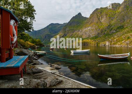 Die malerische Küste des Gebirgssees von Norwegen in der Nähe der Lofoten-Inseln, Fischerboote, die Hänge der Berge mit grünem Gras bedeckt sind Stockfoto