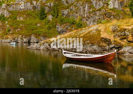 Die malerische Küste des Gebirgssees von Norwegen in der Nähe der Lofoten-Inseln, Fischerboote, die Hänge der Berge mit grünem Gras bedeckt sind Stockfoto