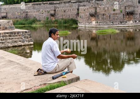Vellore, Tamil Nadu, Indien - 2018. September: Ein indischer Mann, der allein auf den Mauern des alten Vellore Fort sitzt und einen Fluss überblickt. Stockfoto
