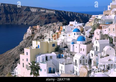 Oia, Santorini, griechische Inseln, Griechenland - Kirchen mit blauen Kuppeln, Häusern und weißen Gebäuden auf Klippen mit Blick auf das Meer bei strahlendem Sonnenschein Stockfoto