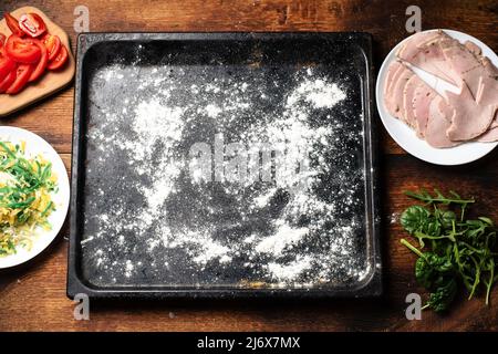 Mehl auf einem Backblech auf einem hölzernen Hintergrund. Vorbereitung für hausgemachte Pizza. Stockfoto