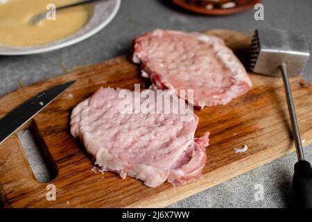 Zwei Stücke geschlagenen Fleisches auf einem Schneidebrett. Kochen von Schweinekoteletts. Stockfoto