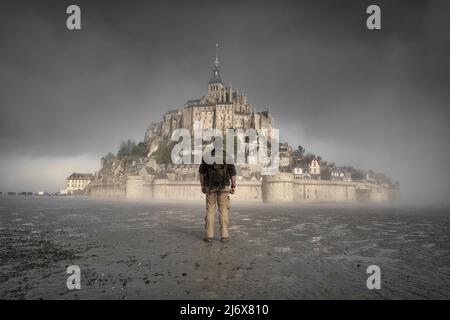 Ein nebliger Morgen auf dem mont saint michel in der normandie, frankreich, Wanderer, der das Kloster betrachtet Stockfoto