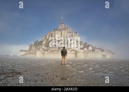 Ein nebliger Morgen auf dem mont saint michel in der normandie, frankreich, Wanderer, der das Kloster betrachtet Stockfoto