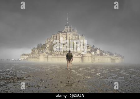 Ein nebliger Morgen auf dem mont saint michel in der normandie, frankreich, Wanderer, der das Kloster betrachtet Stockfoto