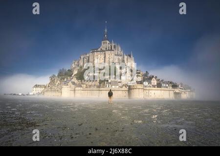 Ein nebliger Morgen am mont saint michel in der normandie, frankreich, Wanderer, der das Kloster anschaut, blauer Himmel Stockfoto