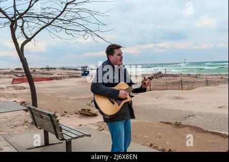 Straßenmusiker, der Gitarre spielt und am Strand von Stearns Park in Ludington, Michigan, USA, singt. Stockfoto