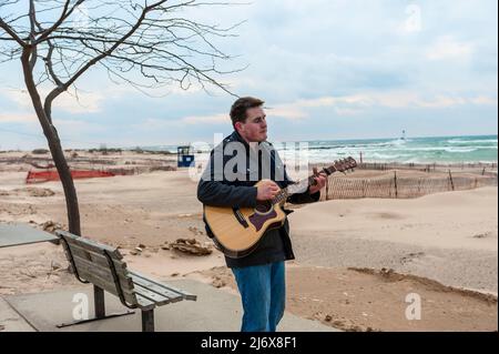 Straßenmusiker, der Gitarre spielt und am Strand von Stearns Park in Ludington, Michigan, USA, singt. Stockfoto