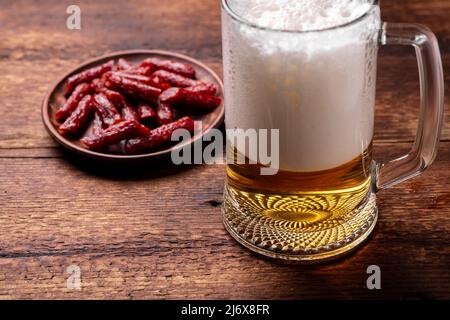 Ein Glas Bier und Snacks - getrocknete Würstchen auf einem Holzhintergrund. Stockfoto