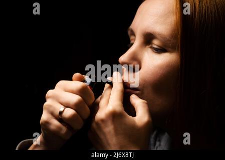 Frau raucht Marihuana, Cannabis durch ein Gerät auf schwarzem Hintergrund. Stockfoto