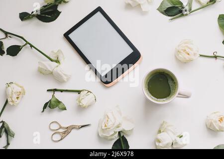 Florale Komposition mit digitalem Tablet, weiße Rosen auf weißem Hintergrund. Minimaler Schreibtisch im Home Office. Flatlay, Draufsicht. Kopieren Sie die Space-Mockup-Vorlage. Stockfoto