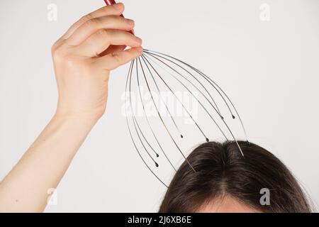 Eine Frau mit einem flexiblen Massagegerät aus Metall zur Selbstmassage des Kopfes auf weißem Hintergrund, kopieren Sie den Ort für den Text Stockfoto