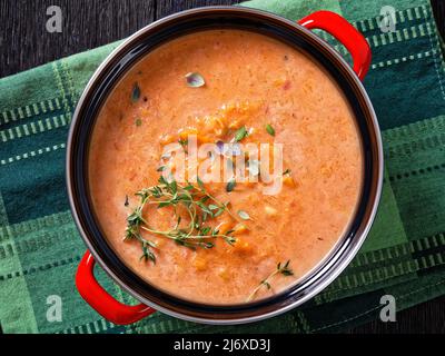 Geröstete Süsskartoffel- und Karottensuppe mit Gemüse im roten Topf auf einem dunklen Holztisch, horizontale Ansicht von oben, flach liegend, Nahaufnahme Stockfoto