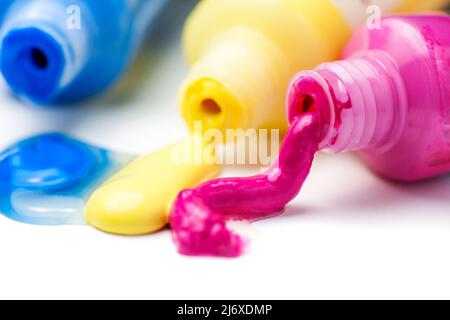 Nahaufnahme von drei offenen Tuben mit magentafarbenen, gelben und blauen Künstlerfarben, die auf weißem Hintergrund auslaufen. Stockfoto