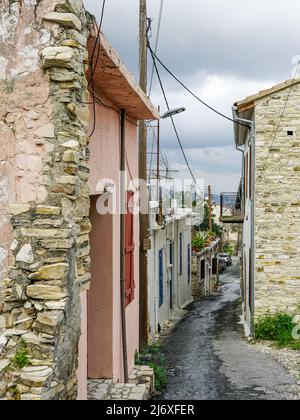 Blick auf eine romantische schmale Straße mit alten Kalksteinhausmauern in einem kleinen, teilweise unbewohnten Bergdorf auf Zypern Stockfoto