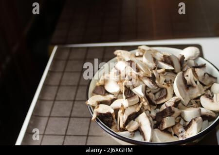 Defokussieren Sie rohe Pilze in der Schüssel auf dunklem Hintergrund in der Küche. Viele schneiden Champignon für Pizza. Veganes Konzept. Nicht fokussiert. Stockfoto