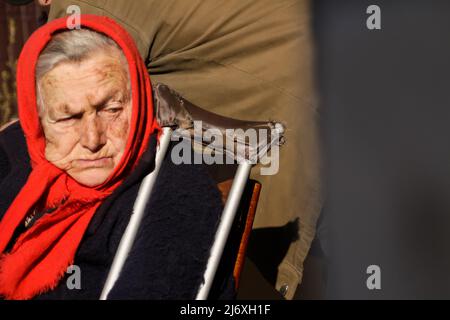 Defokussieren sie die ältere ukrainische Frau in einem roten Schal mit Krücken, die draußen sitzen. Frau 80 Jahre alt. Einzelperson. Nahaufnahme Porträt. Krank und heimatverbunden. Cop Stockfoto