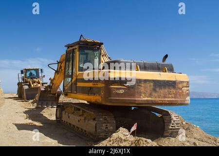 Yellow Raupenbagger arbeitet an der Reparatur einer Straße in den Bergen in der Nähe des Meeres Stockfoto