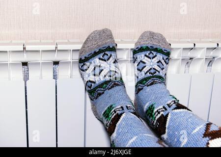 Eine Frau wärmt ihre gefrorenen Füße in Socken auf einer Batterie. Das Konzept der Wärme im Haus. Kalte Jahreszeit Stockfoto