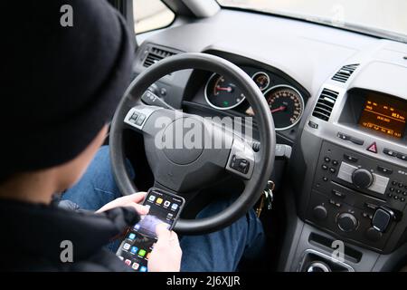Der Fahrer hält das Lenkrad nicht mit den Händen. Er schaut in sein Smartphone Stockfoto