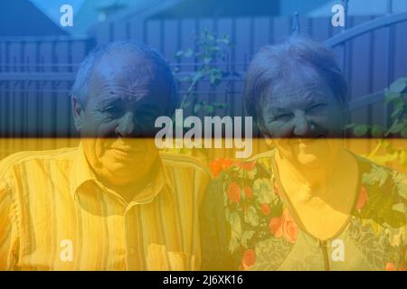 Flagge der Ukraine. Porträt eines älteren Paares, das am Sommertag lächelt. Glückliches älteres Paar von Mann und Frau sitzen auf Blumen Garten Hintergrund. 60s oder 70 Stockfoto