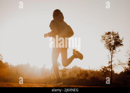 Silhouette eines kenianischen Läufers, der auf einer roten Schotterstraße in der Nähe der Stadt Iten in Kenia läuft. Sportfoto für Langstrecken- und Marathonläufer Stockfoto