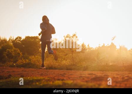 Silhouette eines kenianischen Läufers, der auf einer roten Schotterstraße in der Nähe der Stadt Iten in Kenia läuft. Sportfoto für Langstrecken- und Marathonläufer Stockfoto