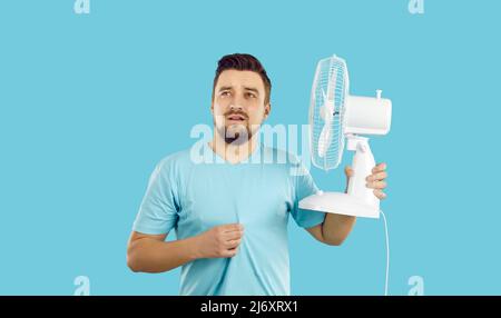 Der Mensch leidet unter Sommerhitze, fühlt sich extrem heiß an, nutzt einen elektrischen Ventilator, schwitzt aber immer noch Stockfoto